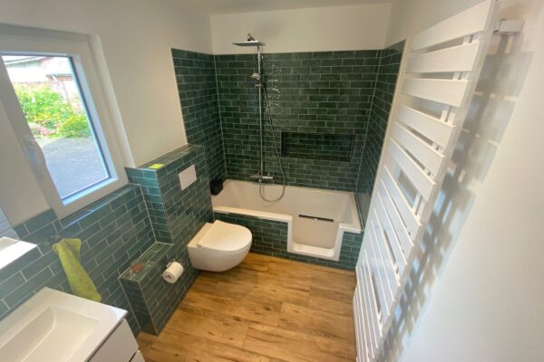 Bild eines Badezimmers mit grünen Fließen an der Wand und weißer Badewanne.